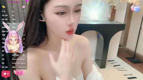 Media: A video of a young Asian woman with fair skin and long, straight black hair, wearing a white off-shoulder top, posing indoors with a digital filter overlay of a pink rabbit.