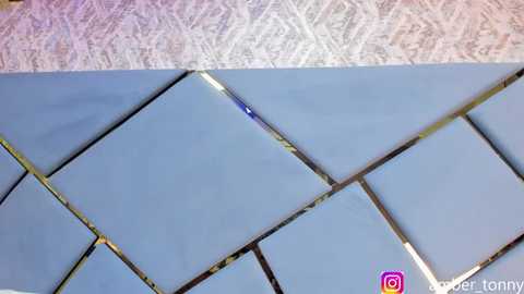 Media: A video showing a close-up of a light blue ceramic tile with a broken edge, set against a background of textured wallpaper. The image has a watermark with the @amber_tommy handle.