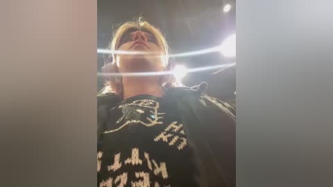 Media: Video of a blonde woman wearing a black and white patterned sweater, captured from a low angle with bright light creating a lens flare effect, creating a dramatic, surreal atmosphere.