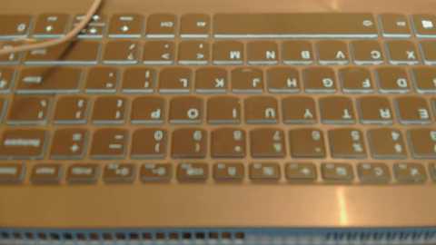 Media: Video of a laptop keyboard featuring a brownish metallic finish with white lettering, including the \"F\" keys and number pad. The keys are slightly glossy, and a white USB cable is plugged into the side.