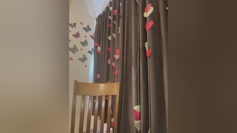 Media: Video of a cozy nursery with a wooden crib, beige walls, and a dark brown curtain with heart and butterfly decals, giving a soft, whimsical feel.