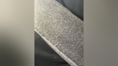 Media: Close-up video of a textured, woven fabric with a smooth, light grey surface, partially visible on a dark grey background, showcasing fine details of the weave.