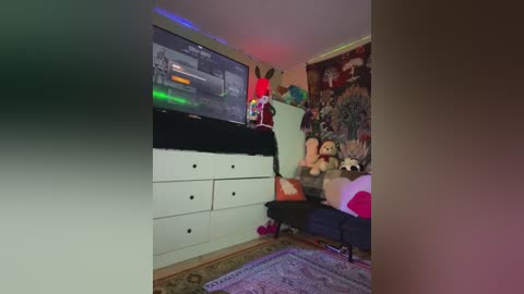 Media: A dimly lit, colorful video of a cluttered bedroom with a large TV, stuffed animals, and a plush chair, featuring a vibrant, multi-colored light strip.