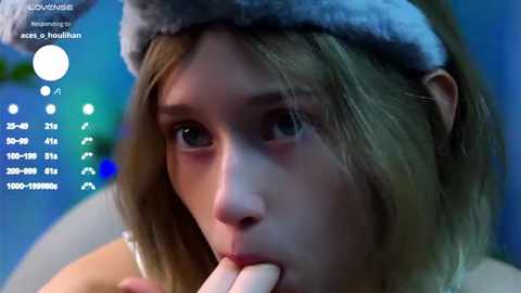 Media: Video of a young woman with light skin and long, blonde hair, wearing a fuzzy blue hat, looking pensive, with a blue and green background, featuring a white text overlay with stats.