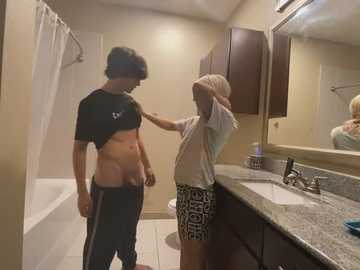 Media: Video of a young man and woman in a bathroom, the woman lifting her shirt to expose her breasts, while the man looks on.