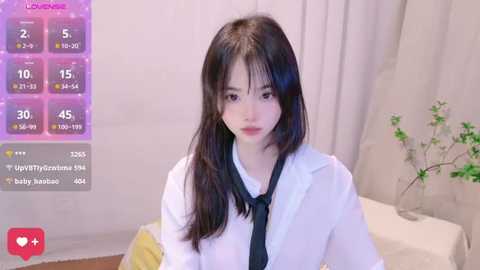 Media: Video of an East Asian woman with long, straight black hair and pale skin, wearing a white shirt and black tie, in a cozy bedroom with light beige curtains and a potted plant.