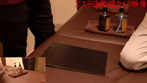 Media: Video of a massage table with a black heating pad, bottles, and towels on a brown tray. Japanese text at the top.