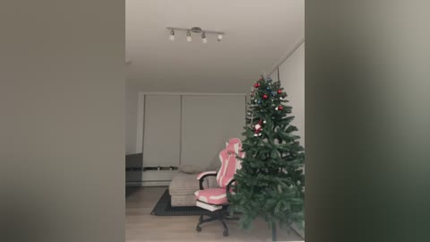 Media: Video of a modern living room with beige walls, a white couch, a pink gaming chair, and a decorated Christmas tree.