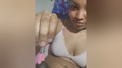 Media: A video of a young woman with light brown skin and a small, round face, wearing a pink lace bra, holding a pink nipple clamp.