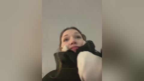 Media: Video of a young woman with fair skin, brown hair, and a black coat, wearing a pink sweater. She is licking a black and white ice cream cone. Background is blurred.