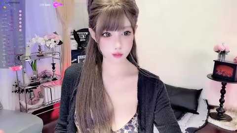 Media: Video of a young East Asian woman with long, straight brown hair in a side ponytail, wearing a black cardigan over a leopard-print bralette. Background includes a bed, flowers, and a TV, creating a cozy, intimate bedroom setting.