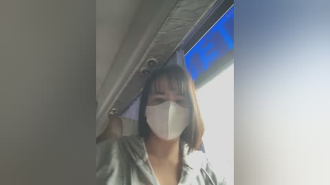 Media: Video of an Asian woman with short brown hair, wearing a gray hoodie and a white mask, inside a plane cabin.