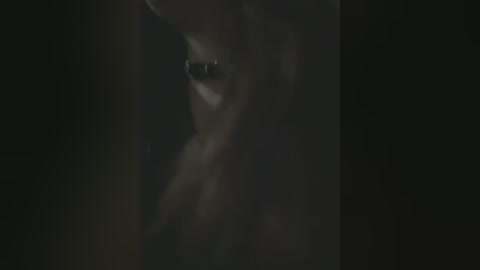 Media: A dimly lit, close-up video of a person's eye and cheek, with a piercing, dark gaze. The background is dark and blurry, creating a moody, intimate atmosphere.