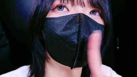 Media: A video of an Asian woman with straight black hair and light skin, wearing a black face mask, blue eyeshadow, and a white top.