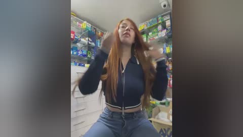 Media: Video of a curvy, fair-skinned woman with long red hair in a grocery aisle, wearing a black jacket and blue jeans, holding a shopping basket, surrounded by colorful packaged goods.