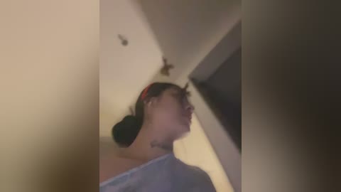 Media: A blurred video of a woman with medium skin tone, dark hair, wearing a red headband and light blue shirt, looking upwards in a dimly lit room.