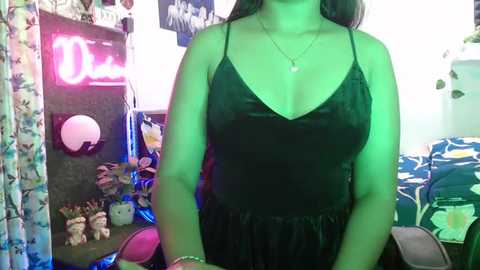 Media: Video of a woman in a black spaghetti strap dress, standing in a cluttered room with neon lights, toys, and colorful curtains.