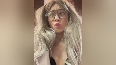 Video of a blonde woman with long, wavy hair, wearing oversized glasses and a white jacket, making a surprised face.