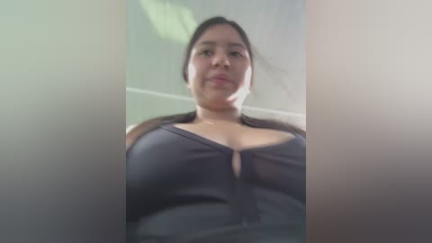 Media: A blurry video of a Latina woman with long dark hair, wearing a black tank top, taken from a low angle. The background is indistinct.