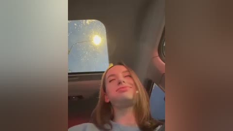 Media: A video captures a young woman with long, light brown hair, smiling while looking out a car window at a sunny sky with a golden sun.