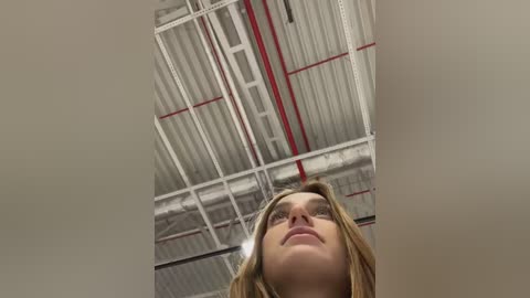 Media: Video of a blonde woman looking up at a high ceiling with white beams and red accents, taken from a low angle.