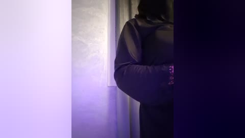 Media: A video of a person in a dark, hooded sweatshirt standing in a dimly lit room with a glowing window, creating a moody, mysterious atmosphere.