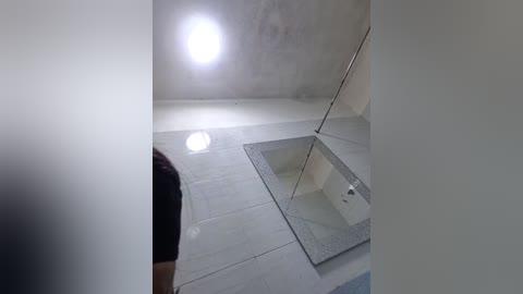 Media: Video of a modern, minimalist bathroom with a glass door leading to a shower, featuring light-colored tiles and a bright, circular light fixture on the ceiling.