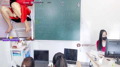 Media: Video of a classroom with a teacher in a red shirt and mask standing in front of a whiteboard, while students sit at desks with laptops.