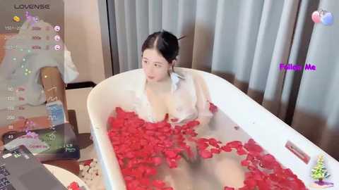 Media: A young East Asian woman with long black hair in a white robe bathes in a white bathtub filled with red rose petals.