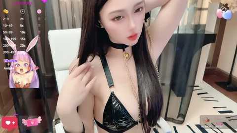 Media: A video of an East Asian woman with long black hair and fair skin, wearing a black leather bra, black choker, and gold chain, posing seductively indoors.