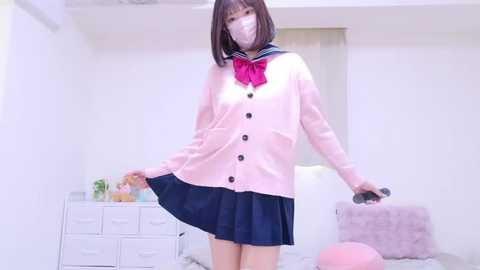 Media: Video of an Asian woman in a pink sailor uniform, mask, and dark skirt, posing in a brightly lit, minimalist bedroom.