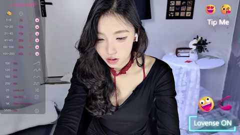 Media: A video of an Asian woman with long black hair and fair skin, wearing a black top and red choker, captured in a modern bedroom setting.