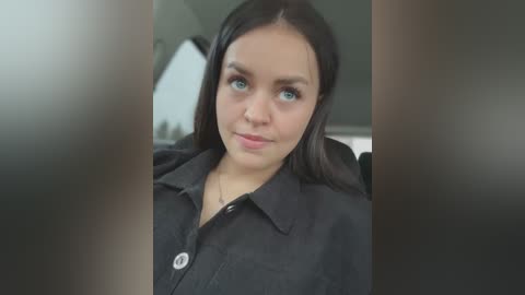 Media: Video of a young woman with fair skin, blue eyes, and straight black hair, wearing a black shirt, seated in a car, blurred background.