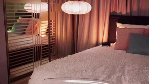 Media: Video of a cozy bedroom with a white, textured bedspread, beige curtains, wooden slat wall, and hanging lanterns.