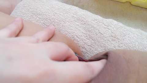 Media: A close-up video of a light-skinned person's hand gently pressing a beige, textured towel against their lower abdomen. The image focuses on the tactile sensation and softness of the fabric.