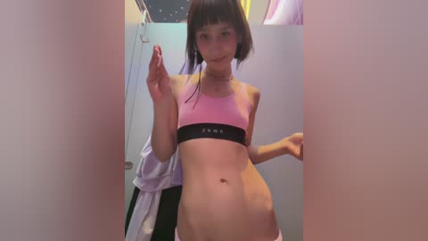 Media: Video of a slender, light-skinned woman with a bob haircut, wearing a pink sports bra and pink panties, posing confidently in a narrow, mirrored hallway.