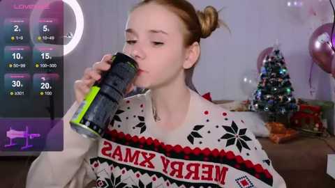 Media: Video of a fair-skinned, blonde girl in a \"Merry Christmas\" sweater, drinking a can, in a festive living room with a decorated Christmas tree.