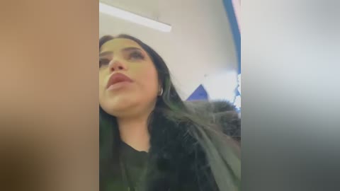 A low-quality, grainy video of a woman with long black hair and full lips, wearing a black top, taken from a low angle.