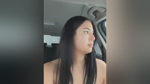 Media: Video of a young woman with long black hair, fair skin, and a slender physique, seen from the side in a car, looking contemplative.