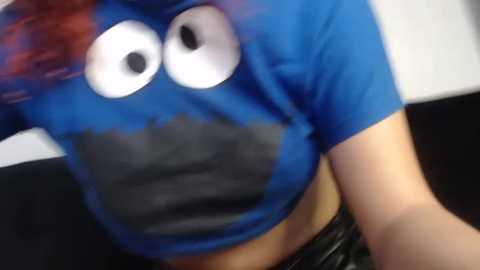 Media: A blurry video of a person wearing a blue t-shirt with a large, black mouth covering the chest and oversized white eyes on the shoulders. The background is indistinct.