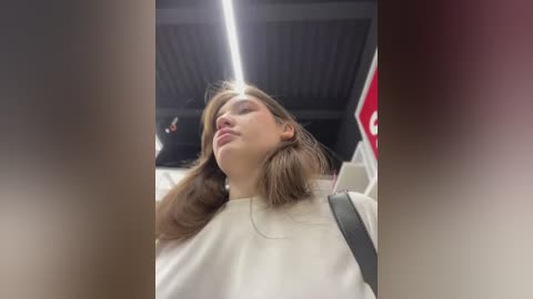 Media: Video of a young woman with light brown hair, wearing a white shirt, reclined in a car with a red stop sign in the background.