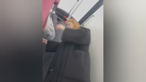 Media: A blurry video of a woman in a black coat and a red bag inside a train compartment, with a pink and black background.