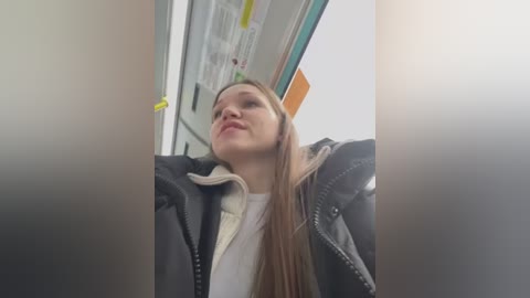 Media: A candid video of a young woman with long brown hair, wearing a black jacket and white shirt, taken from a low angle inside a vehicle.