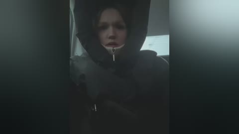 Media: A video of a young woman in a dimly lit car, wearing a hooded jacket with her mouth open, possibly crying.