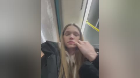 Media: A blurred video of a young woman with long blonde hair, wearing a black jacket, wiping her nose on her hand inside a public restroom.