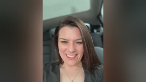 Media: Video of a smiling woman with long brown hair, wearing a black top, inside a car, with blurred interior background.