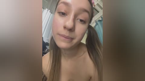 Media: Video of a young woman with light skin, brown pigtails, and a neutral expression, wearing a strapless top, in a bathroom with a white shower curtain.