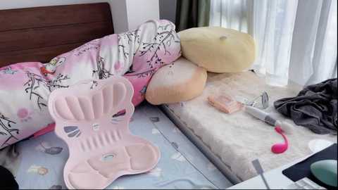 Media: Video of a cluttered bedroom with a pink crib, stuffed animals, a baby bottle, and a white stuffed pillow on a bed covered in pastel bedding.