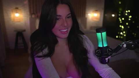 Media: Video of a smiling, dark-haired woman with long hair, wearing a low-cut top, singing into a microphone in a dimly-lit room with warm lighting and Christmas lights.