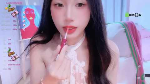 Media: A video of an East Asian woman with long black hair, pale skin, and red lipstick, licking a lollipop while topless. Background includes a whiteboard with health information and a pink blanket.